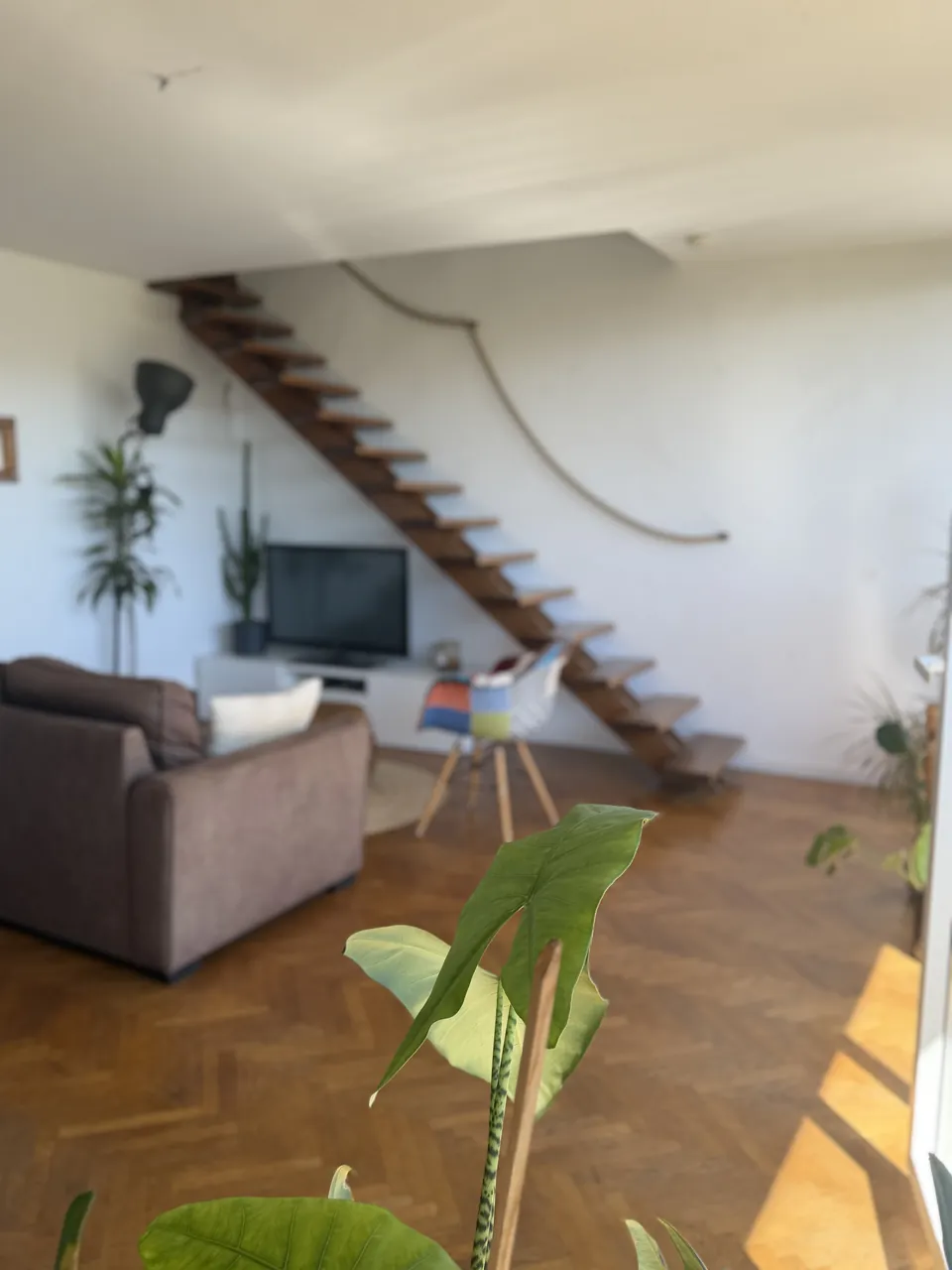 Séjour baigné de soleil avec parquet en chevrons et escalier en bois, prêt à accueillir les voyageurs